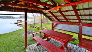 A covered picnic area with benches and a table, overlooking a body of water.