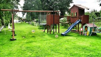 Un parque infantil con columpios, tobogán, estructura para escalar y una casita.