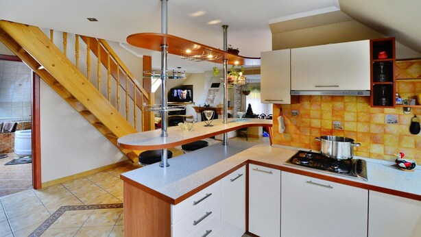 A kitchen with a wooden staircase, white cabinets, a gas stove, and a tiled backsplash. - Cottage by Ostrowieckie Lake With Private Beach (Malechowo)