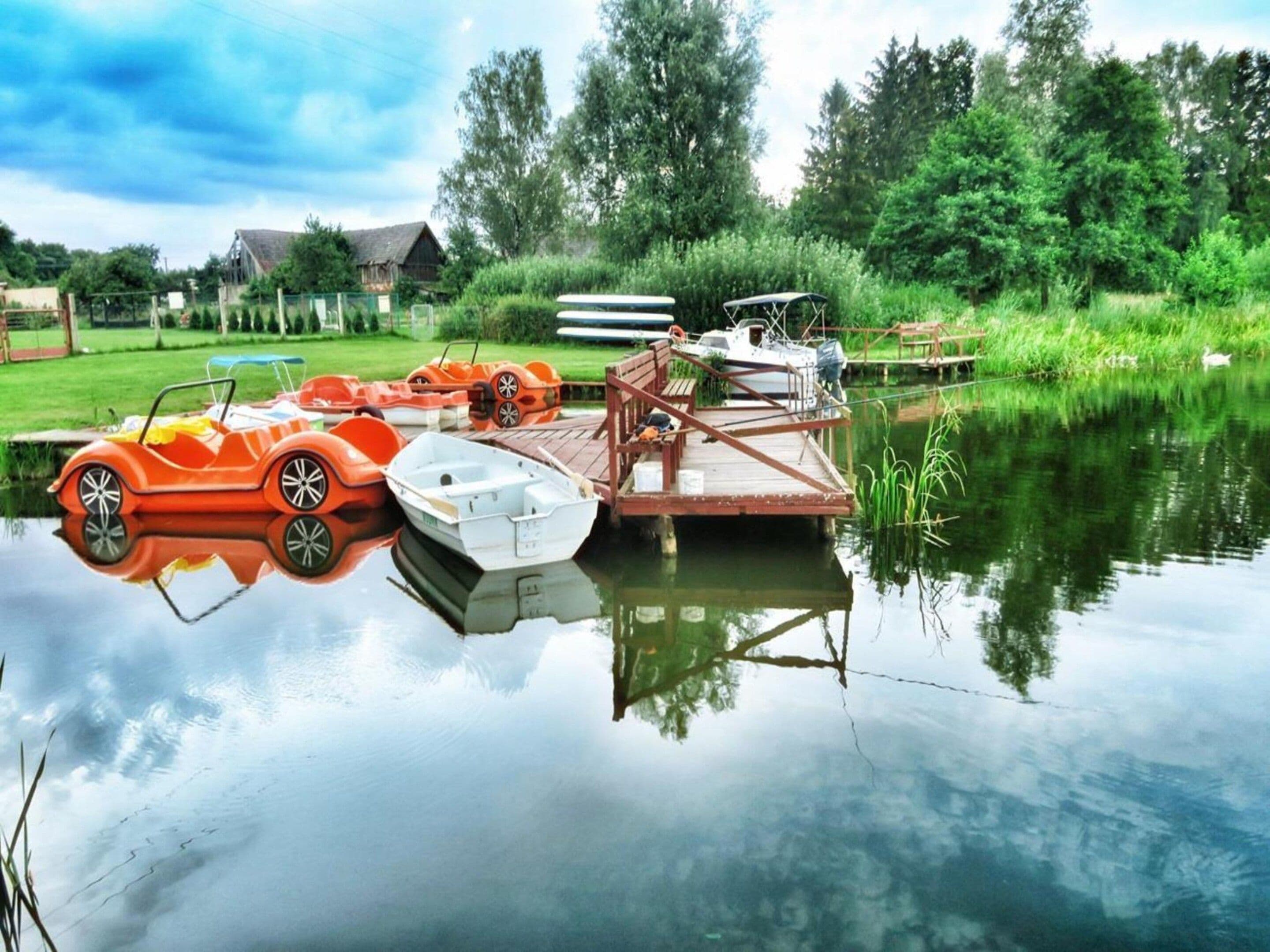 A calm water body with boats docked, surrounded by greenery and a wooden structure.