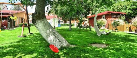 A well-maintained garden with a swing set, a hammock, and a red disc.