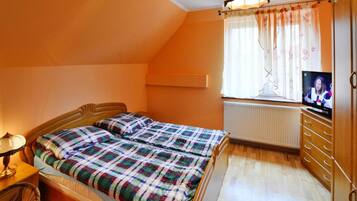 A bedroom with a bed, a television, a dresser, and a window with curtains.