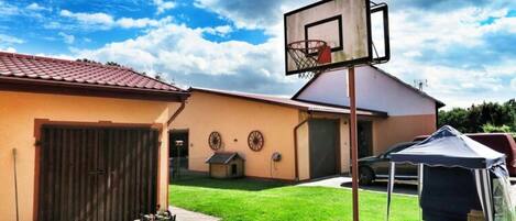 A residential backyard with a basketball hoop, a covered play tent, and a brick patio.