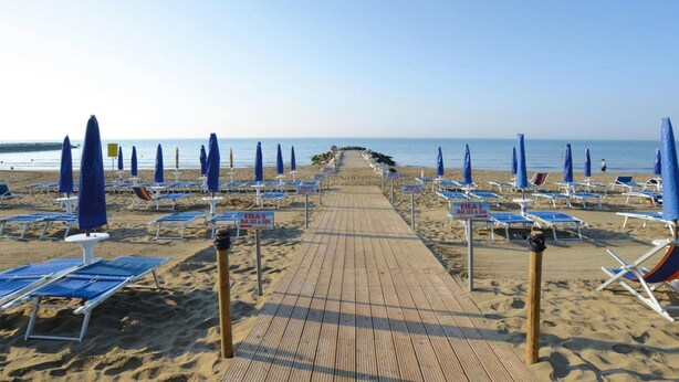 Une plage avec une promenade en bois qui mène à des rangées de chaises longues et de parasols bleus.