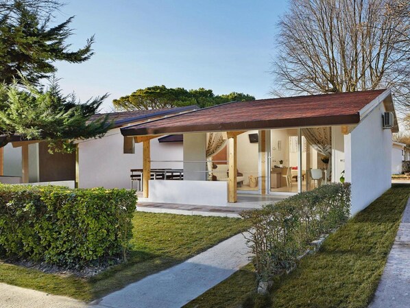 A modern single-story house with a covered porch, a visible kitchen area, and a well-maintained lawn. - Bungalow in Caorle With Garden Furniture (Caorle)