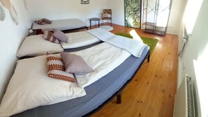 Ein Zimmer mit zwei Betten, einem kleinen Tisch, einem Stuhl und einem großen Fenster.