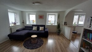 Ein modernes Wohnzimmer mit einem dunkelgrauen Ecksofa, einem runden Couchtisch und einer Bücherwand voller Bücher.