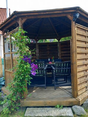 A wooden gazebo with a table and chairs, surrounded by greenery and rocks. - Ferienwohnung mit Garten in Reisbach Nähe Bayernpark (Reisbach)