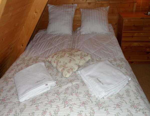 A neatly made bed with floral bedding, two pillows, and folded towels on a wooden floor. - Holiday Homes With Terraces, Close to the Beach (Mielno)