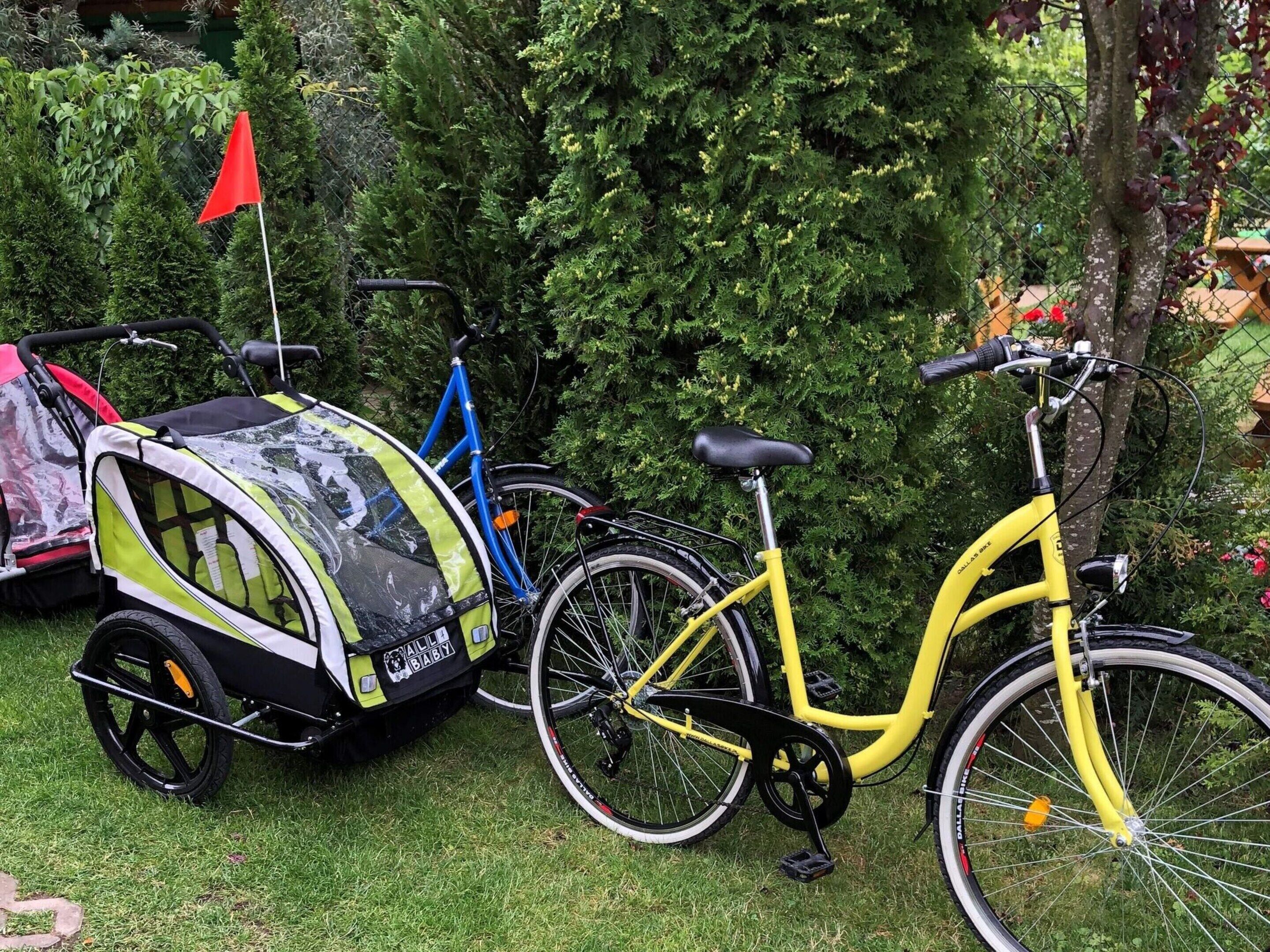 A yellow bicycle with a child bike trailer attached, parked on a grassy area with a red flag on top.