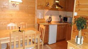 A wooden interior with a dining table and chairs, a kitchen with a microwave and sink, and a small potted plant. - Holiday House in Sarbinowo Near the Beach (Mielno)