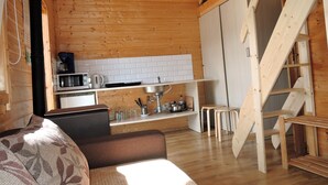 Interior acogedor de una cabaña con detalles de madera, un sofá, una zona de cocina con microondas y una escalera de madera.