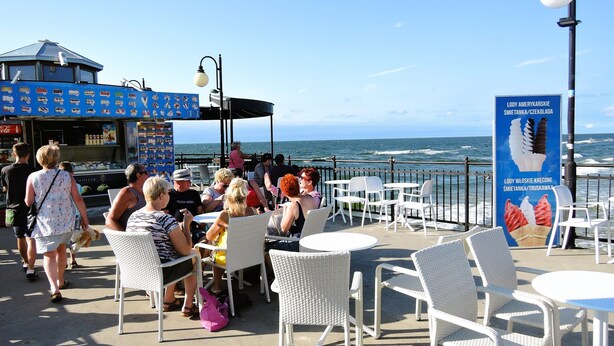 Un café frente al mar con terraza, un carrito de comida y vistas al océano.