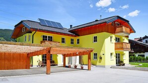 Ein gelbes Gebäude mit einem hölzernen Balkon und Solaranlagen auf dem Dach.