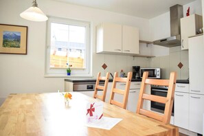 Une cuisine moderne avec des meubles blancs, une table à manger en bois et une fenêtre donnant sur des immeubles.