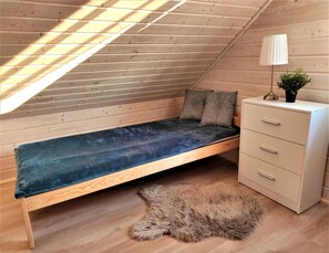 Een kleine kamer met een schuin dak, een enkel bed, een kapstok en een lamp.