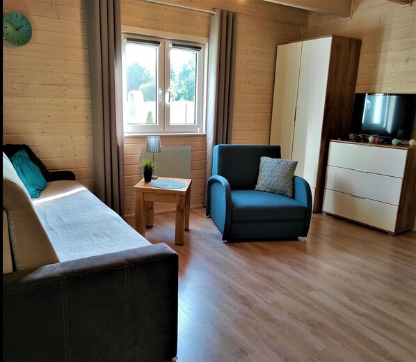 Une pièce comprenant un lit, une chaise, une petite table avec une lampe, un téléviseur et une armoire.