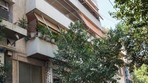 Un edificio de varios pisos con gimnasio en la planta baja, coches aparcados y un árbol en la fachada.