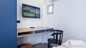 Una habitación con un escritorio de madera, una silla negra, un reposapiés marrón y una toalla blanca sobre la cama.