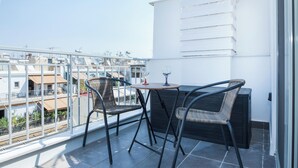 A balcony with a table and two chairs, a glass of wine, and a view of surrounding buildings. - Athens Studio Escape with Balcony (Athens)