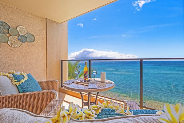 Uma varanda com mobiliário de vime, uma mesa com garrafa e copos, e vista para o oceano.