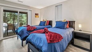 Un dormitorio con dos camas, una mesita de noche, una silla y una mesa con vistas a árboles.