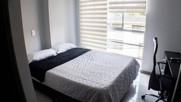 A bedroom with a bed, a desk, and a window with blinds.