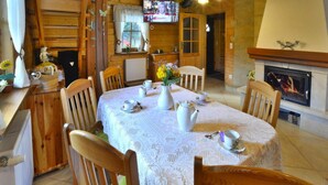 A cozy log cabin interior with a dining table set for tea, wooden chairs, a fireplace, and a television mounted on the wall. - Holiday Home by the Lake, Private Garden, Oswino (Chociwel)