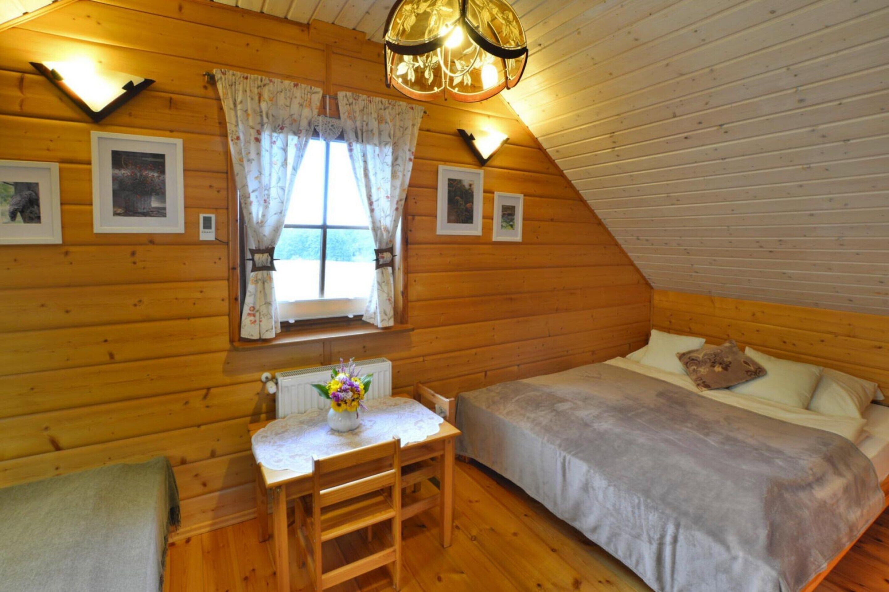 Una habitación de cabaña acogedora con una cama, una mesa con un florero y cuadros en las paredes.