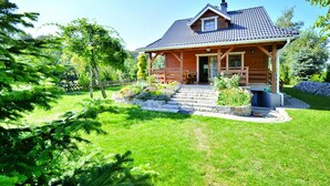 A wooden cabin with a sloped roof, a porch, and a stone pathway leading to the entrance. - Holiday Home by the Lake, Private Garden, Oswino (Chociwel)