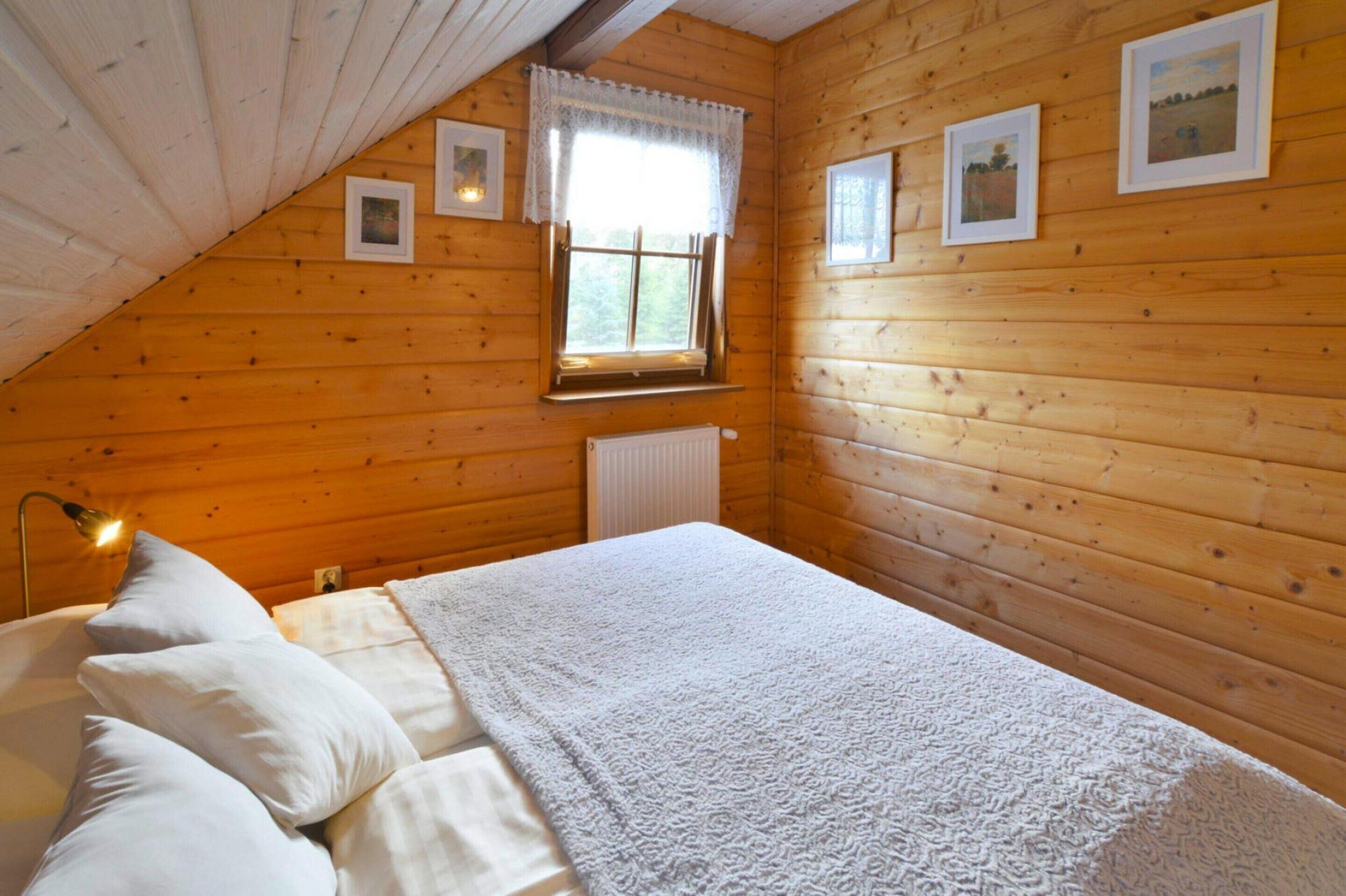 Un dormitorio acogedor con techo de madera, cama con ropa blanca, radiador y cuadros en la pared.
