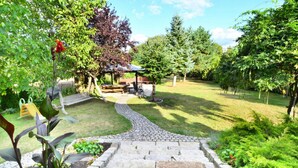 A garden with a paved pathway leading to a gazebo, surrounded by lush greenery and trees. - Holiday Home by the Lake, Private Garden, Oswino (Chociwel)
