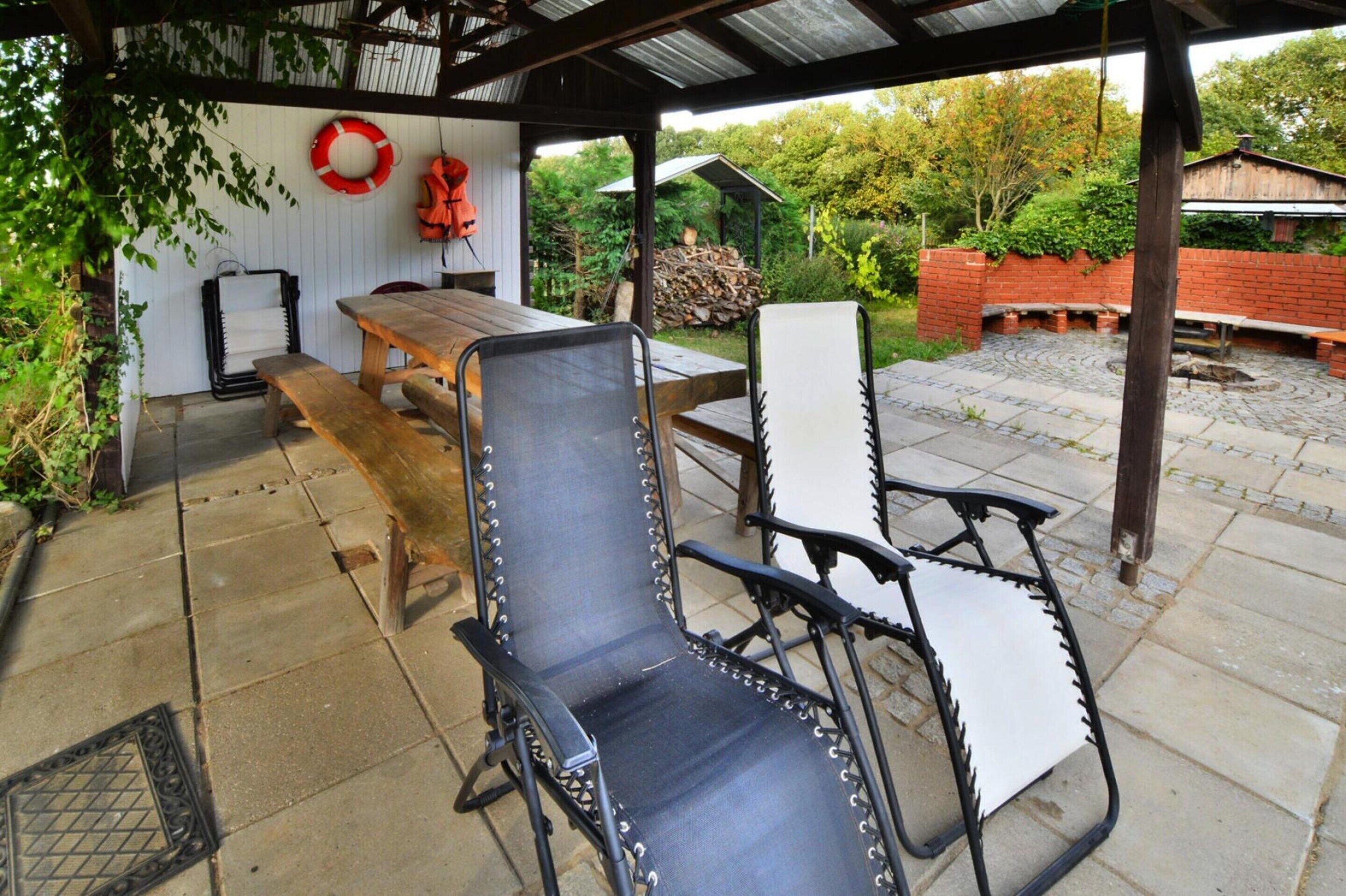 Eine überdachte Terrasse mit einem Holztisch und Metallstühlen, umgeben von einer Ziegelmauer und Grünpflanzen.