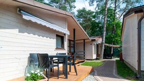 A wooden cabin with a covered patio, outdoor seating, and a gravel path leading to a gate. - Holiday Cottages, Sauna, Whirlpool, Mrzezyno (Trzebiatow)