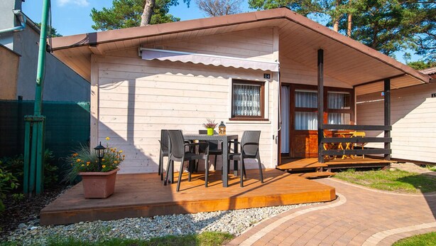 A single-story wooden house with a patio area featuring a table and chairs. - Holiday Cottages, Sauna, Whirlpool, Mrzezyno (Trzebiatow)