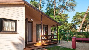 A wooden cabin with a porch, a bench, and a playground. - Holiday Cottages, Sauna, Whirlpool, Mrzezyno (Trzebiatow)