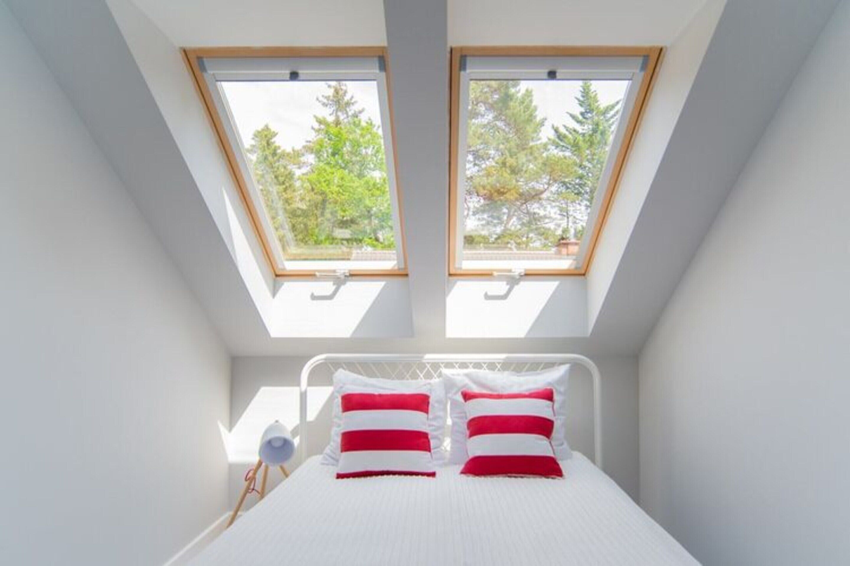 A bedroom with a skylight, a bed with white bedding and red and white pillows, and a bedside lamp.