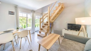 Un salon moderne avec un escalier en bois, un coin repas comprenant une table et des chaises, un canapé, un téléviseur et une lampe.