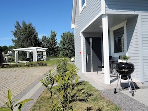 Et hus med en overdækket terrasse, grill og en have.