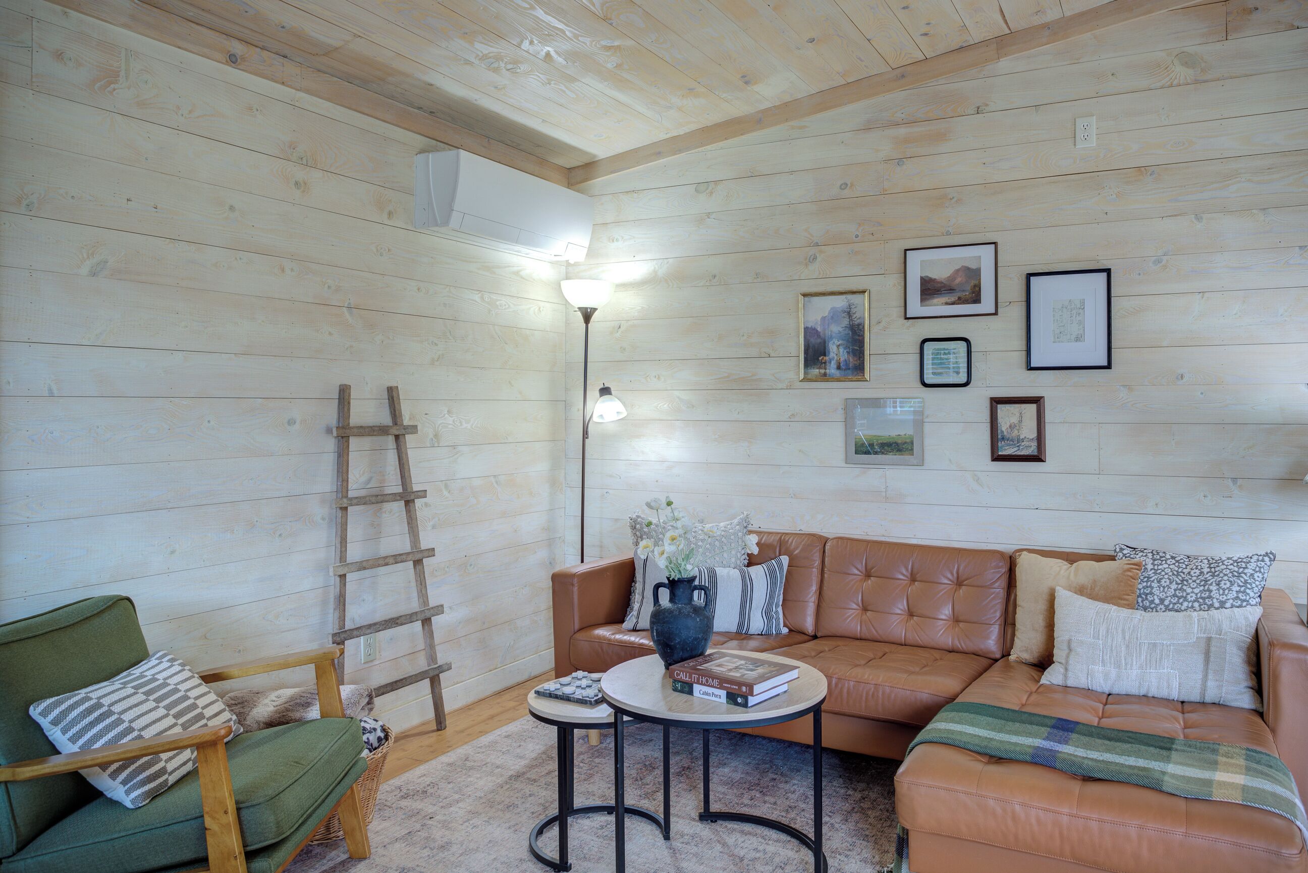 Un accogliente soggiorno con pareti in legno, un divano in pelle, una poltrona verde, un tavolino da caffè e una lampada da terra.