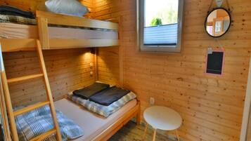 A compact wooden cabin room with bunk beds, a small round table, and a window with blinds.