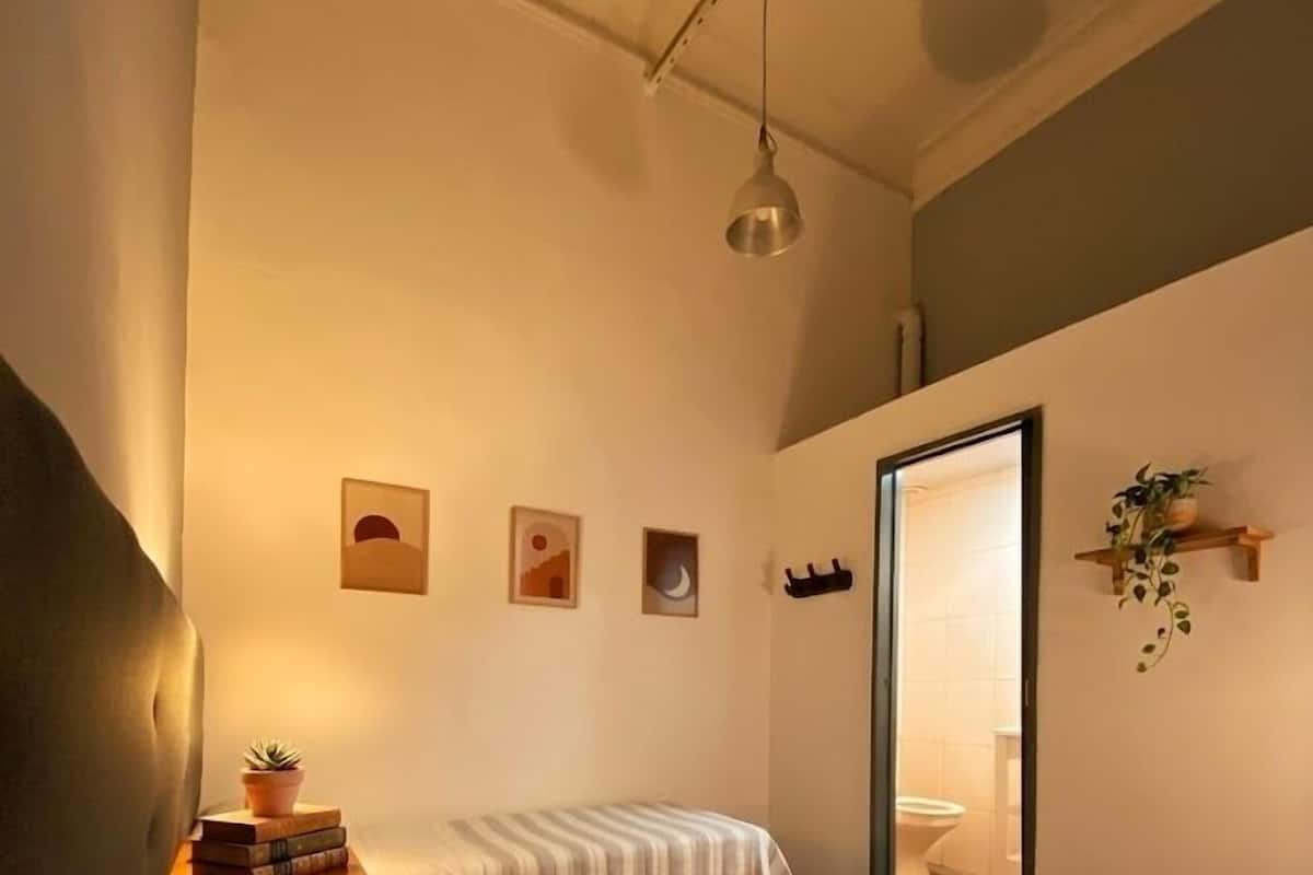 A bedroom with two beds, a bedside table with a plant, and a hanging light fixture.