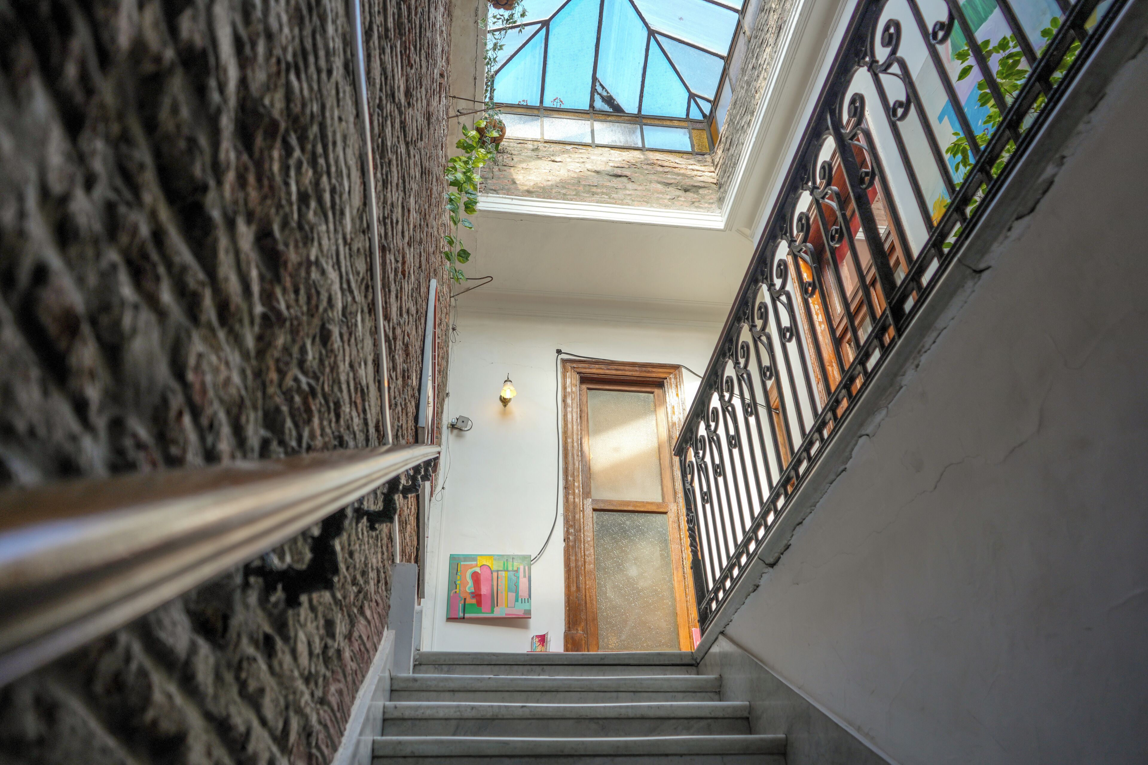 Una escalera estrecha con barandilla de metal, una puerta de madera al final y un pequeño ventanal con vista al cielo.