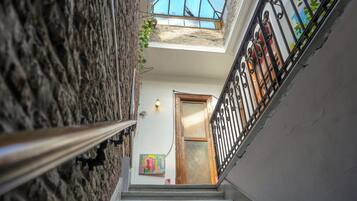 Una escalera estrecha con barandilla de metal, una puerta de madera al final y un pequeño ventanal con vista al cielo.