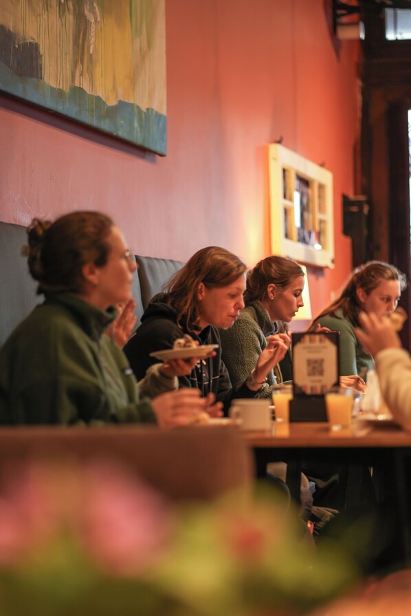 A group of people seated at a table in a restaurant with a red wall and a painting above them. - ViaVia BsAs GuestHouse (Buenos Aires)