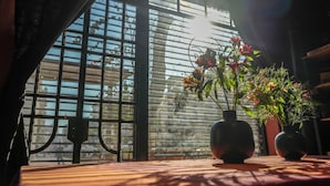 Een kamer met een groot raam, twee vazen met bloemen en een tafel met een tafelkleed met patroon.