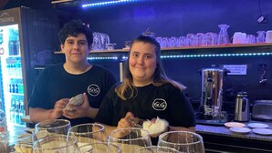 Twee personen aan een bar met een tafel vol lege wijnkaraffen.