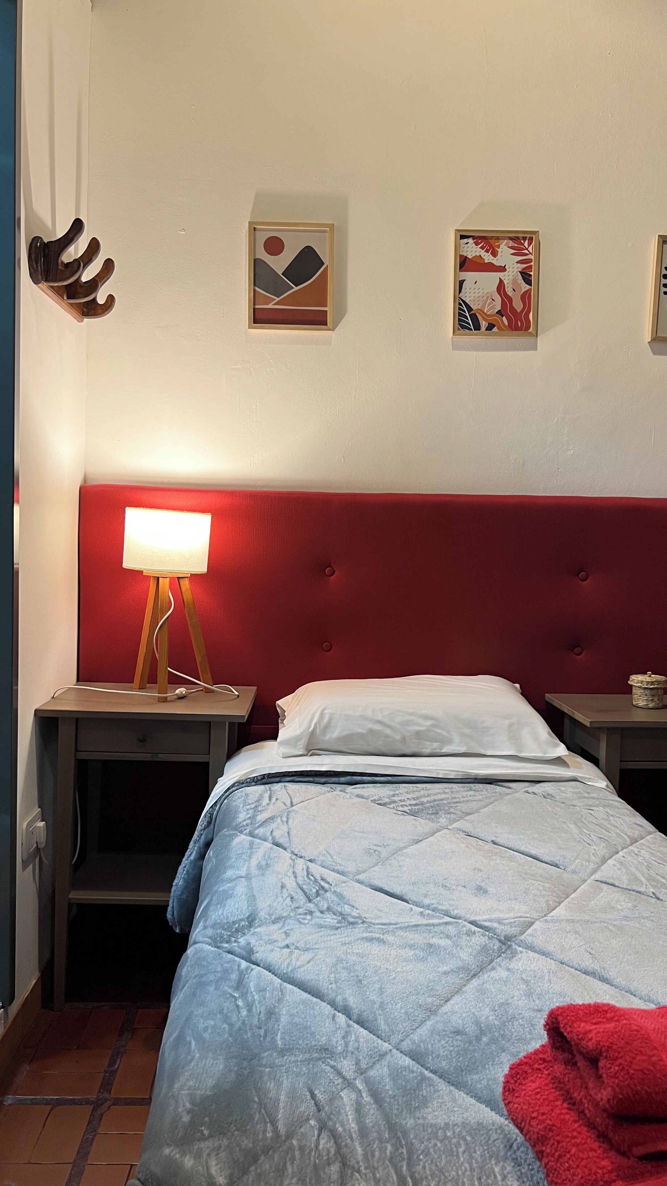 A bedroom with a red headboard, a bedside table with a lamp, a bed with a blue quilt, and two framed pictures on the wall.