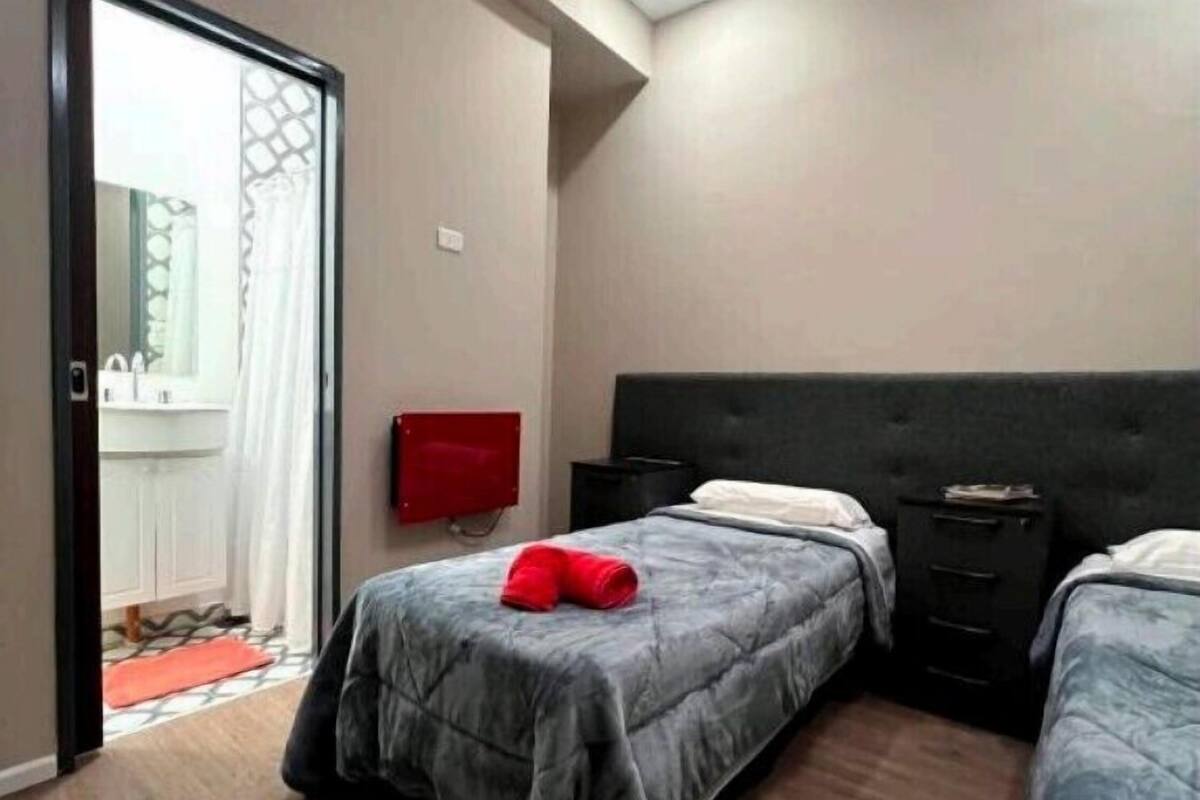 A room with two beds, a red fire alarm, a TV, and a sliding door leading to a bathroom.