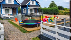 A vacation property with two blue houses, a trampoline, and a play area with colorful toys. - Holiday Home in Rewal Near Baltic Sea Beach (Rewal)
